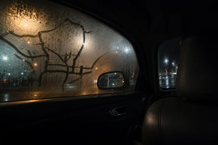 Interno di un'auto ferma di notte, con mappa stradale bagnata e finestrino appannato