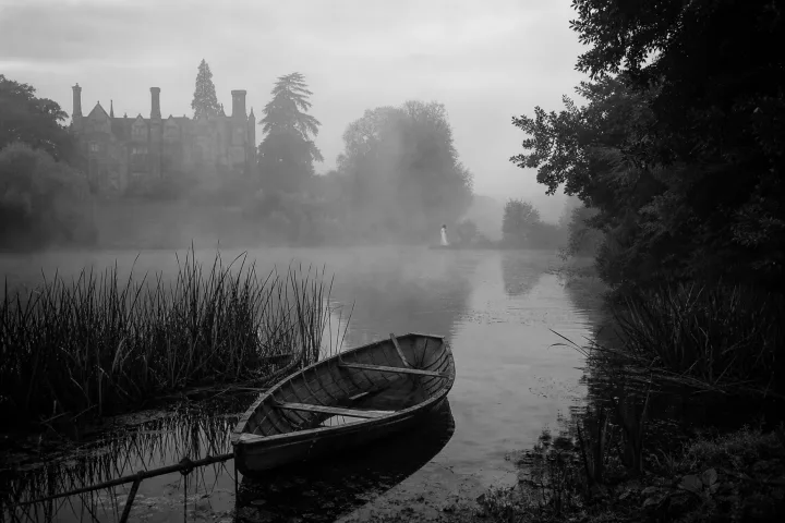 Un lago nebbioso accanto a una dimora inglese, con una presenza lontana appena visibile tra i vapori