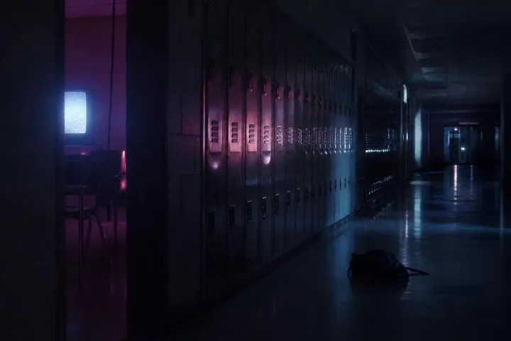 Corridoio scolastico notturno con luce rosa e blu proveniente da un'aula aperta