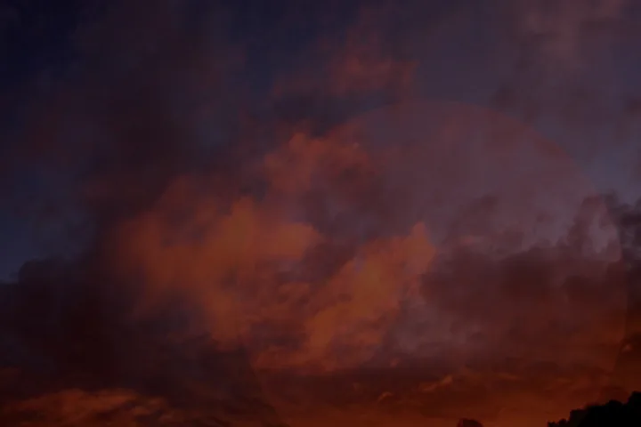 Cielo scuro e rossastro sopra una collina, con nuvole dense che sembrano trattenere una luce caduta